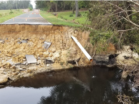 A large gap in the road by one of our sampling sites where flooding washed out a bridge, and an exposed pipe leaking fluid into the stream.