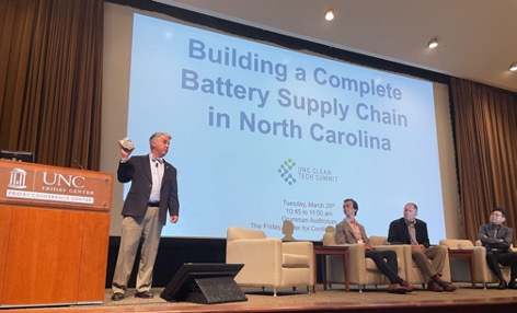 Dr. Jeff Warren moderating a panel with employees of Ford, Piedmont Lithium, and Soelect; Jeff is holding a rock containing spodumene ore, a source of lithium.
